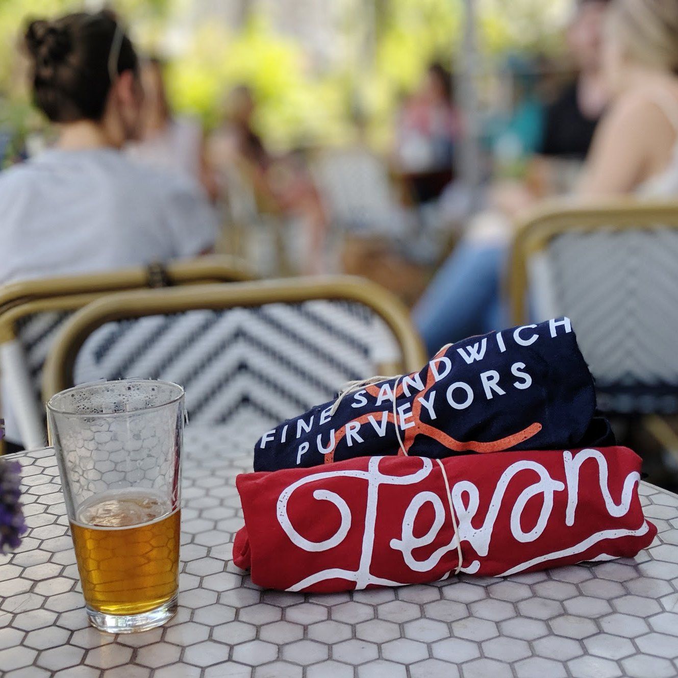 a beer and two t-shirts sitting on a Leven patio table during a sunny happy hour